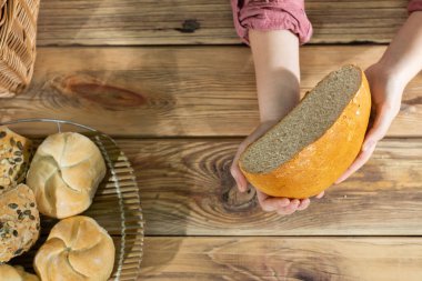 Kadınların elleri, yuvarlak buğdaylı ekmeğin yarısını ahşap tezgahın üzerinde tutar..