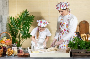 Kız, su ve yumurta oranını dengelemek için fazladan buğday unu serpiyor. Anne ve bebek mutfakta hamuru birlikte yapıyorlar..