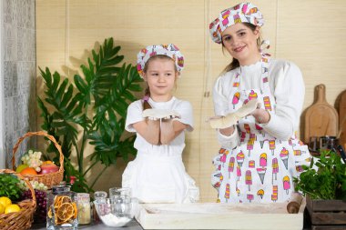 Güzel anne ve beş yaşındaki kızı, her biri pizza hamuru sarılmış olarak ellerini kaldırdılar. Anne ve bebek mutfakta hamuru birlikte yapıyorlar..
