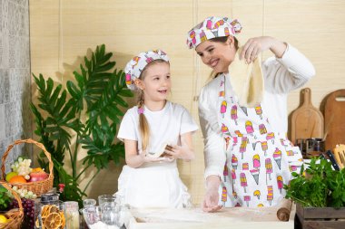 Güzel anne ve beş yaşındaki kızı, her biri pizza hamuru sarılmış olarak ellerini kaldırdılar. Anne ve bebek mutfakta hamuru birlikte yapıyorlar..