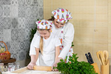 Bir anne ve sevgili kızı birlikte hamuru ince bir pizza hamuruna çevirmek için ahşap bir merdane kullanırlar. Anne ve bebek mutfakta hamuru birlikte yapıyorlar..