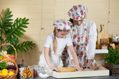 Anne ve kızı pizza hamurunu mutfaktaki bir tahtada tahta bir oklavayla yuvarlıyorlar. Anne ve bebek mutfakta hamuru birlikte yapıyorlar..