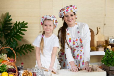 Anne ve kızı pizza hamurunu mutfaktaki bir tahtada tahta bir oklavayla yuvarlıyorlar. Anne ve bebek mutfakta hamuru birlikte yapıyorlar..