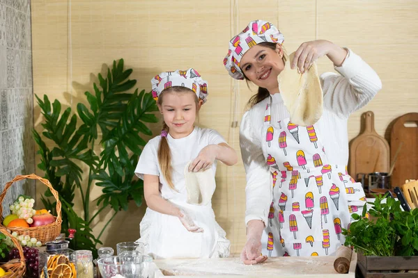 Güzel anne ve beş yaşındaki kızı, her biri pizza hamuru sarılmış olarak ellerini kaldırdılar. Anne ve bebek mutfakta hamuru birlikte yapıyorlar..
