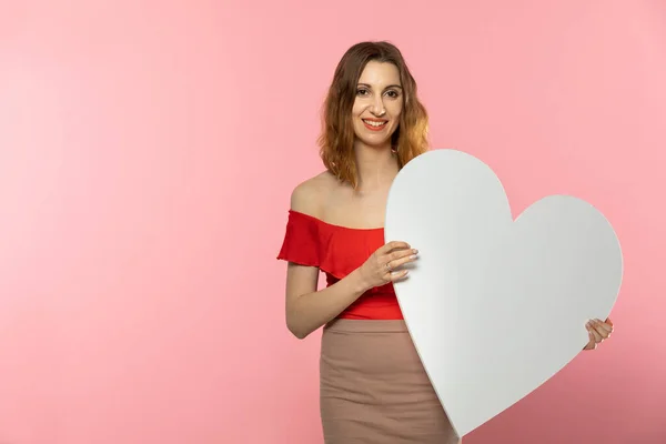 Chica con una gran forma de corazón blanco en las manos. Una estudiante enamorada se para y sostiene una gran forma de corazón en sus manos. Día de San Valentín y amor. — Foto de Stock