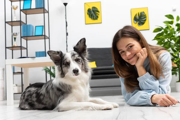 The teen and her dog lie on the floor together, relaxing in their spare time from exercising. Intelligent Border Collie Sheepdog. Modern interior design of the apartment.