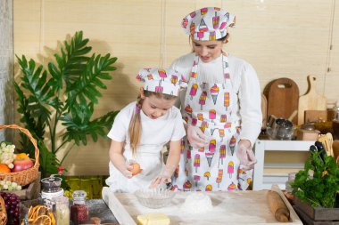 Tavuk öküzünü kırıp hamurun üstündeki yığın halinde duran ellenmiş ve tuzlanmış una eklemek. Anne ve çocuğun mutfak hazırlıklarında ortak çalışmaları.