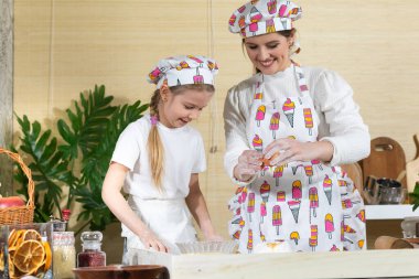 Tavuk öküzünü kırıp hamurun üstündeki yığın halinde duran ellenmiş ve tuzlanmış una eklemek. Anne ve çocuğun mutfak hazırlıklarında ortak çalışmaları.