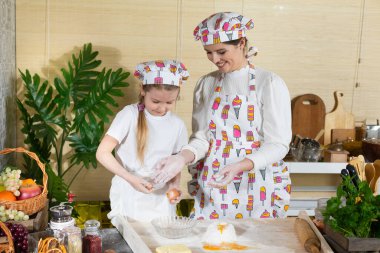 Tavuk öküzünü kırıp hamurun üstündeki yığın halinde duran ellenmiş ve tuzlanmış una eklemek. Anne ve çocuğun mutfak hazırlıklarında ortak çalışmaları.