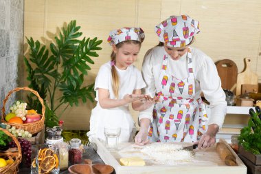 Annem hamuru mutfak bıçağıyla karıştırıyor ve beş yaşındaki kızı da kaşıkla yapıyor. Anne ve bebek mutfakta hamuru birlikte yapıyorlar..