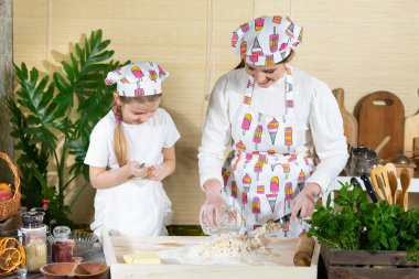 Annem hamuru mutfak bıçağıyla karıştırıyor ve beş yaşındaki kızı da kaşıkla yapıyor. Anne ve bebek mutfakta hamuru birlikte yapıyorlar..