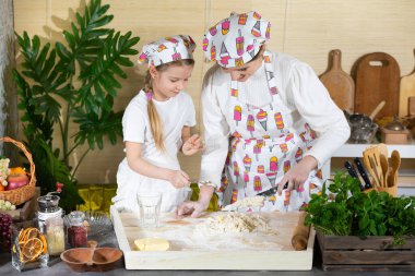 Annem hamuru mutfak bıçağıyla karıştırıyor ve beş yaşındaki kızı da kaşıkla yapıyor. Anne ve bebek mutfakta hamuru birlikte yapıyorlar..