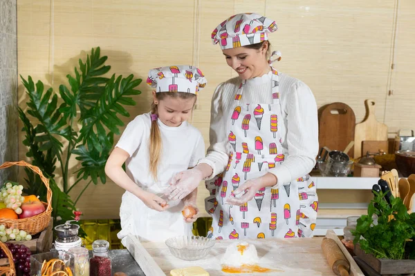 Tavuk öküzünü kırıp hamurun üstündeki yığın halinde duran ellenmiş ve tuzlanmış una eklemek. Anne ve çocuğun mutfak hazırlıklarında ortak çalışmaları.