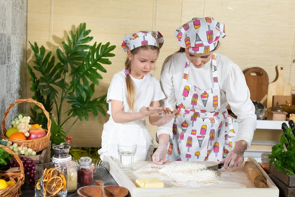 Annem hamuru mutfak bıçağıyla karıştırıyor ve beş yaşındaki kızı da kaşıkla yapıyor. Anne ve bebek mutfakta hamuru birlikte yapıyorlar..