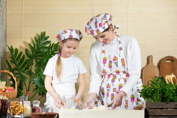 Annem hamuru mutfak bıçağıyla karıştırıyor ve beş yaşındaki kızı da kaşıkla yapıyor. Anne ve bebek mutfakta hamuru birlikte yapıyorlar..