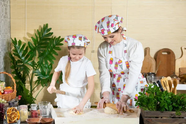 Anne ve kızı pizza hamurunu mutfaktaki bir tahtada tahta bir oklavayla yuvarlıyorlar. Anne ve bebek mutfakta hamuru birlikte yapıyorlar..