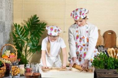 Anne ve kızı pizza hamurunu mutfaktaki bir tahtada tahta bir oklavayla yuvarlıyorlar. Anne ve bebek mutfakta hamuru birlikte yapıyorlar..