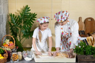 Anne ve kızı pizza hamurunu mutfaktaki bir tahtada tahta bir oklavayla yuvarlıyorlar. Anne ve bebek mutfakta hamuru birlikte yapıyorlar..