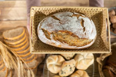 Yakından bakıldığında, örülmüş sepetin içinde bir somun ekmeğin nazikçe eğilip kadın eliyle tutulduğunu görebilirsiniz. Çok nesilli gelenekleri olan aile pastanesi..