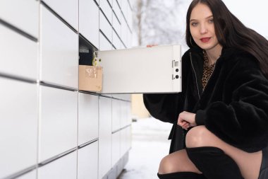 Genç bir öğrenci paket dolabının önünde çömeldi ve posta kutusunun içindekileri kontrol etti. Kışın paketleri otomatik olarak al ve gönder.