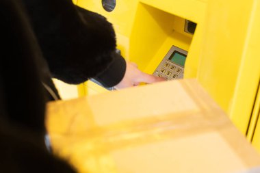 Kadın bir ambalaj dolabının tuş takımını kullanıyor. Kışın paketleri otomatik olarak al ve gönder.