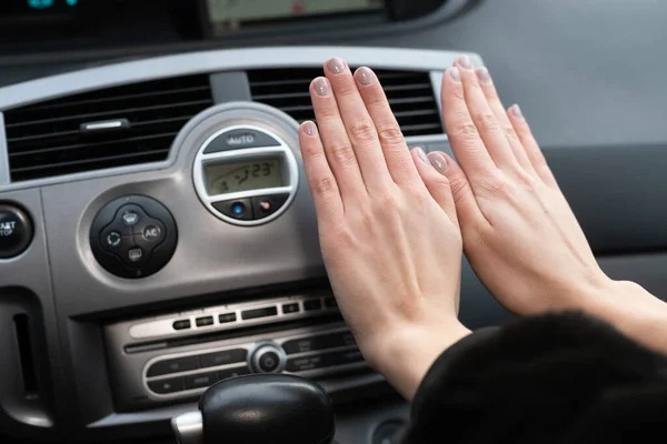 The girl holds her hands over the cars hot air outlet. Cold hands.