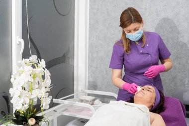 Güzellik uzmanı müşterilerin yüzünü jelden nazikçe temizler ve özel bir gazlı bez kullanır..