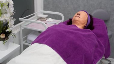 Müşteri kozmetik bir yatakta yüzünde bir alg maskesiyle uzanıyor ve kozmetik aksesuarlarını temizlerken derin derin nefes alıyor.