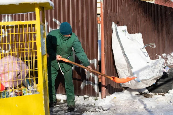 Elle çalışan bir işçi kaldırımdan kar toplar ve yanındaki yığının üzerine atar.