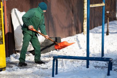 Elle çalışan bir işçi kaldırımdan kar toplar ve yanındaki yığının üzerine atar.