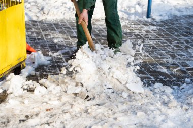 Bir işçi kaldırımdaki donmuş buz parçalarını kırmak için metal kürek kullanıyor.