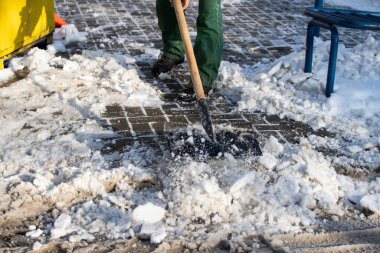 Bir işçi kaldırımdaki donmuş buz parçalarını kırmak için metal kürek kullanıyor.