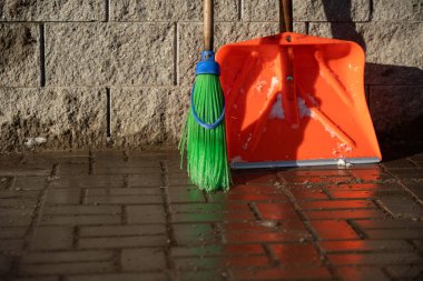 Bir portakal kar küreği ve bir sopa fırçası duvara yaslanıyor.