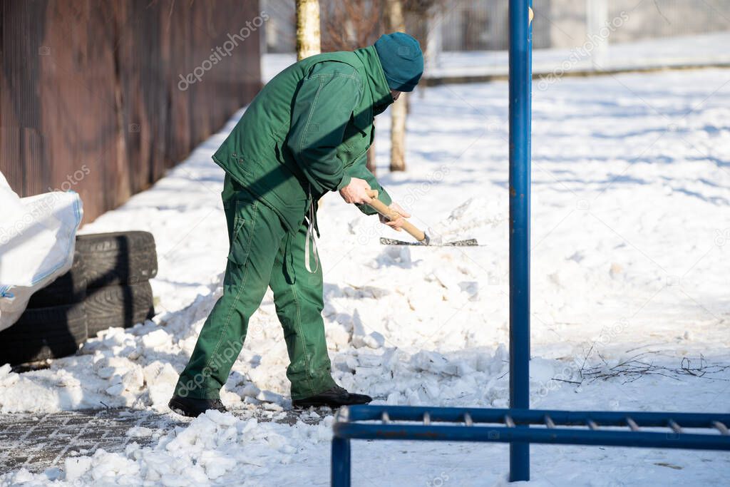 A manual worker scoops snow from the pavement and shovels it onto a pile next to it