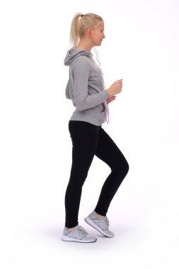 Genç bir kız beyaz bir arka planda koşuyor, yandan bakıyor ve kulaklıkları kulaklığında.