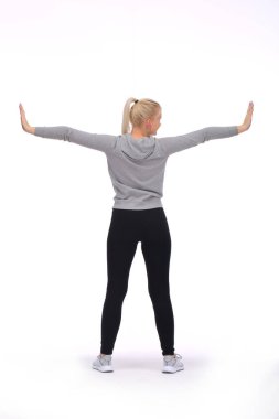 Egzersiz yaparken, genç bir kız kollarını yana açıyor ve yana bakıyor. Arka görünüm