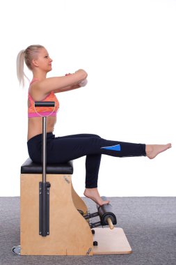 20 yaşındaki antrenör, asansör koltuğunda kolları bağlı ve dik oturarak pilates yapıyor..