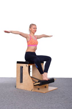 20 yaşında bir antrenör, asansör koltuğunda pilates yapıyor, kollarını omuz hizasına kaldırıyor ve yan tarafına doğru eğiliyor. Oturmuş