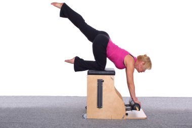 50 yaşında bir bayan antrenör asansör sandalyesinde pilates yapıyor, bacağını başının üstüne kaldırıyor. Kadın dizlerinin ve ellerinin üzerinde dinleniyor.