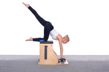 20 yaşında bir bayan antrenör, asansör sandalyesinde pilates yapıyor ve bacağını başının üstüne kaldırıyor. Bir kadın dizinde ve ellerinde dinleniyor.