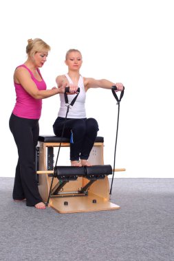 50 yaşındaki antrenör asansör koltuğuna pilates egzersizi öğretiyor. Jimnastik kauçuk kol kaslarının yardımıyla genç bir kız.