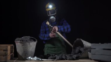Bir madenci bir kazma tutar ve onu bir taraftan diğer tarafa taşır. İş kıyafeti giymiş bir maden işçisi.