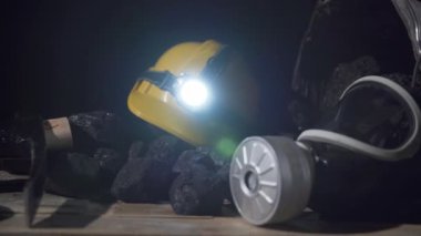Ahşap platformda içinde kömür olan bir kova, filtresi olan koruyucu bir maske ve parlayan bir el feneri olan bir miğfer görebilirsiniz.