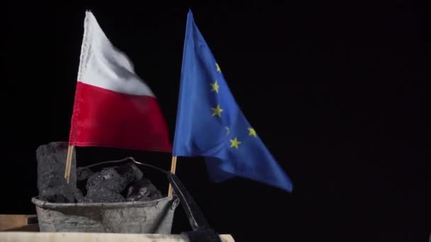 Un cubo lleno de carbón negro sostiene una bandera polaca y una bandera de la Unión Europea, ambas ondeando al viento — Vídeos de Stock