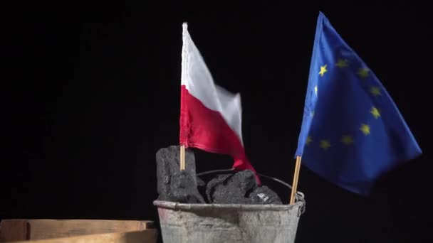 En hink med svart kol rymmer en polsk flagga och en EU-flagga, båda fladdrande i vinden. — Stockvideo