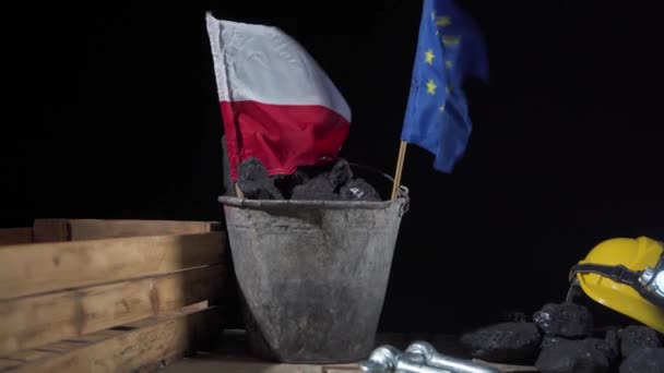 Duas bandeiras, a da Polónia e a da União Europeia, são colocadas num balde cheio de carvão negro, ambas agitadas ao vento. Mineiros capacete com uma lanterna — Vídeo de Stock