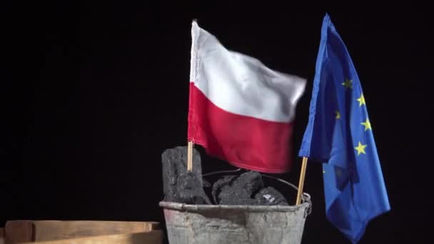 Un cubo lleno de carbón negro sostiene una bandera polaca y una bandera de la Unión Europea, ambas ondeando al viento — Vídeo de stock