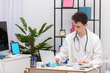 Genç bir ilköğretim hekimi hasta verilerini bir dizüstü bilgisayarın veri tabanına kaydediyor. Doktorun ofisi.