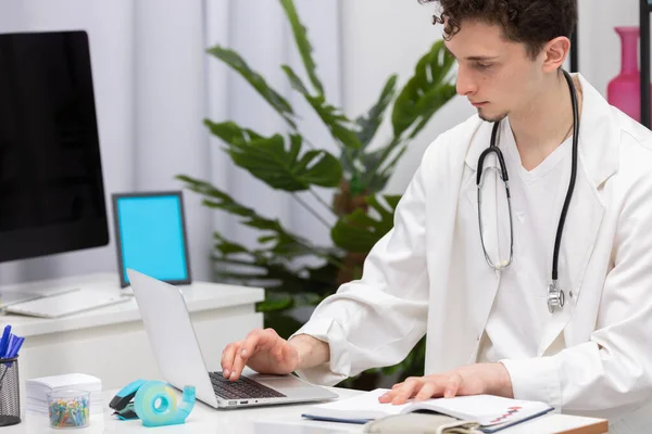 Um jovem médico da atenção primária insere os dados do paciente em um banco de dados de laptop. Serviço de médicos — Fotografia de Stock