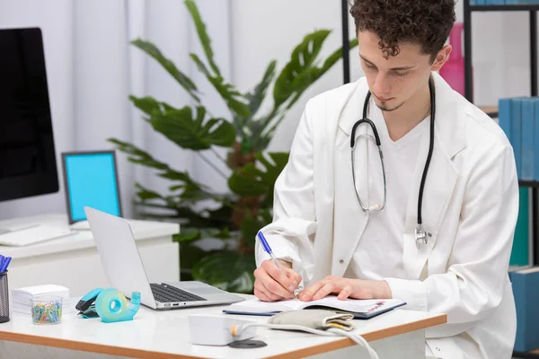 Un joven médico de atención primaria escribe notas de pacientes en un calendario. Oficina de médicos —  Fotos de Stock